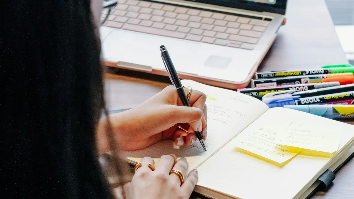 A student taking notes beside a laptop at a desk