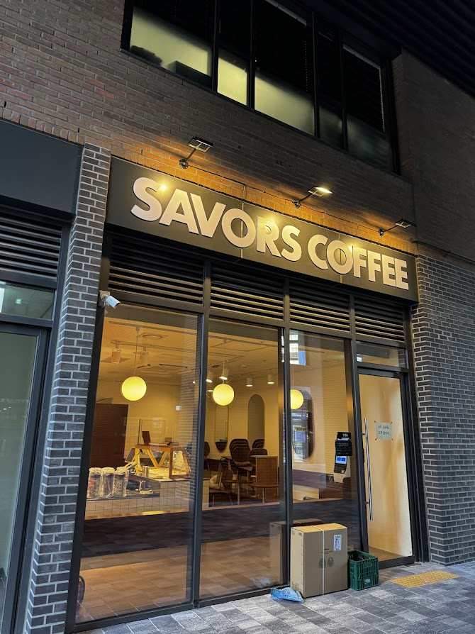 SAVORS COFFEE brick storefront with tall windows and warm globe pendant lights.