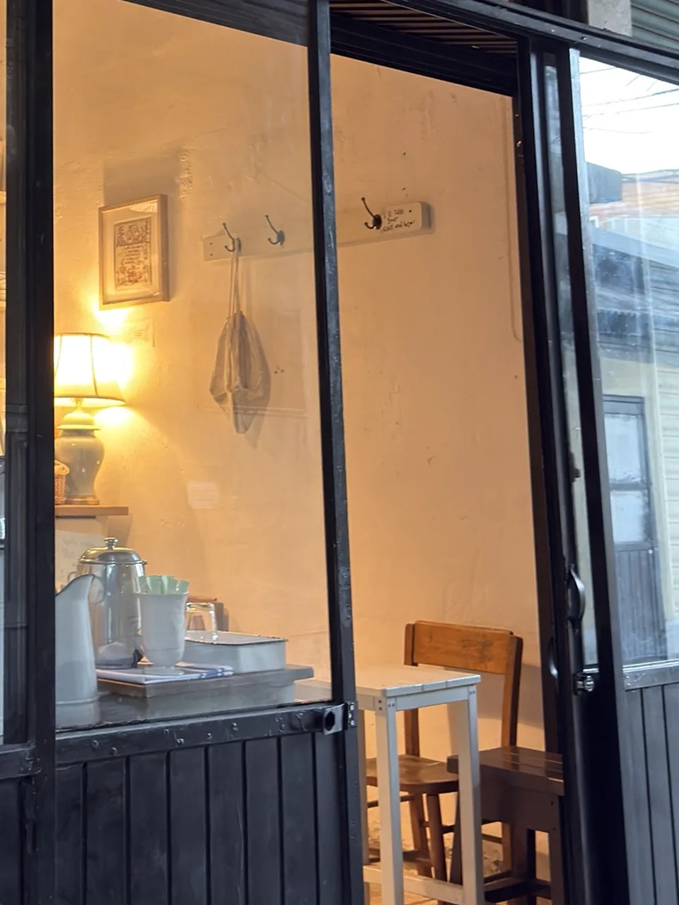 Inside Thomas Bakery: a table lamp, a framed sampler, wall hooks and a small white table with wooden chairs.